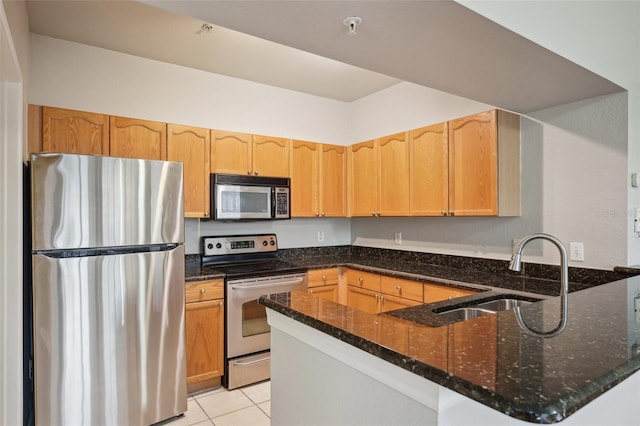 kitchen with dark stone counters, stainless steel appliances, a peninsula, and a sink