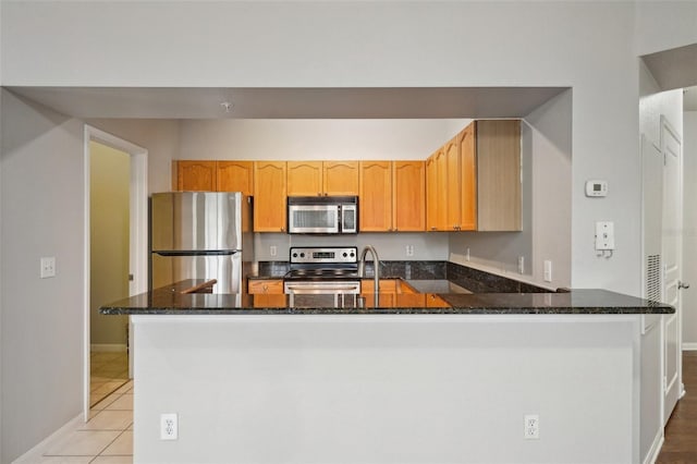 kitchen with light tile patterned floors, baseboards, dark stone counters, appliances with stainless steel finishes, and a peninsula