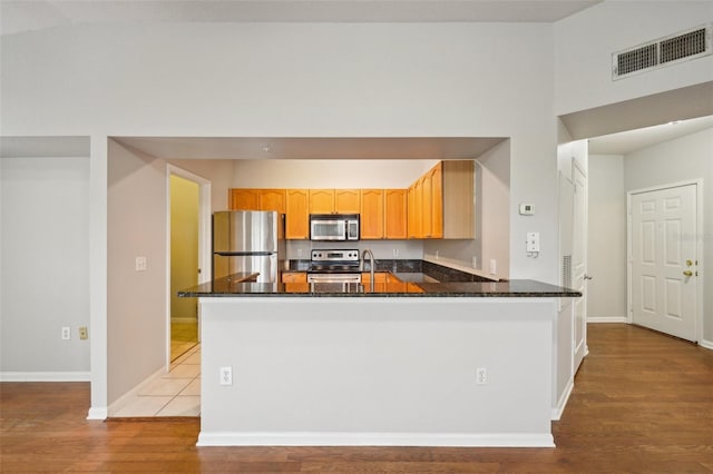 kitchen featuring a peninsula, visible vents, appliances with stainless steel finishes, light brown cabinetry, and light wood finished floors