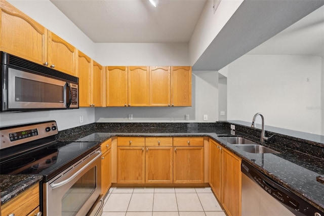 kitchen with appliances with stainless steel finishes, dark stone counters, light tile patterned flooring, and a sink