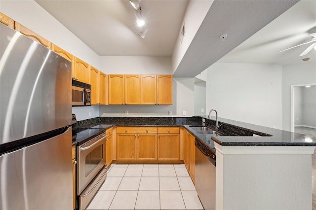 kitchen with light tile patterned floors, stainless steel appliances, a peninsula, a sink, and dark stone counters