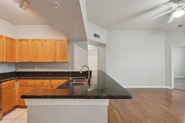 kitchen featuring a sink, a ceiling fan, visible vents, baseboards, and dark stone countertops