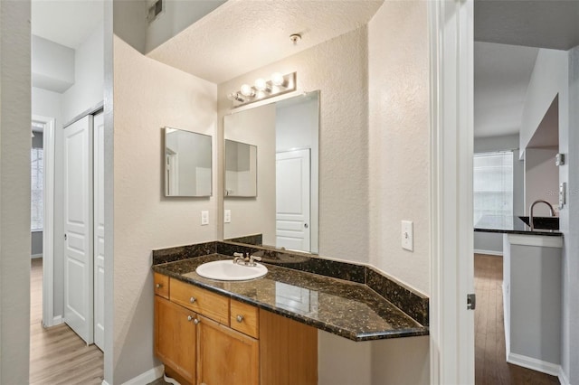 bathroom featuring visible vents, baseboards, a textured wall, wood finished floors, and vanity