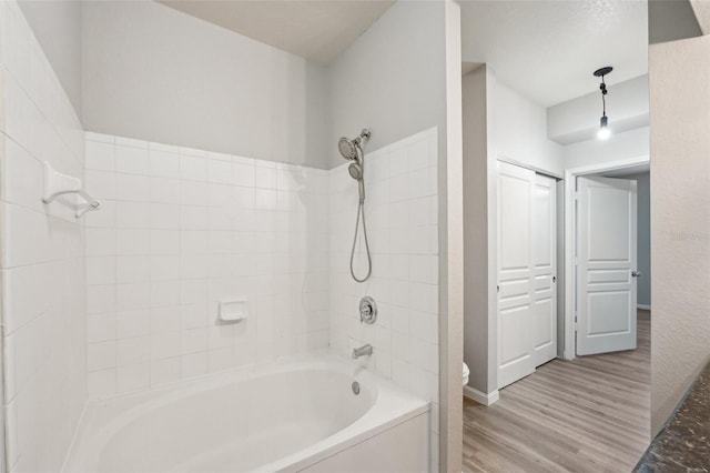 bathroom featuring toilet, baseboards, shower / washtub combination, and wood finished floors