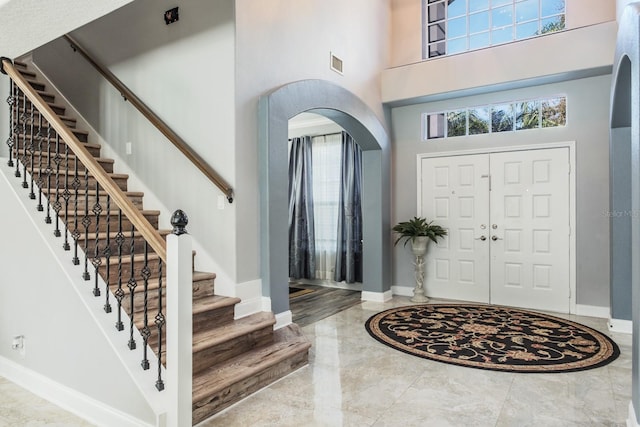 foyer with arched walkways, marble finish floor, baseboards, and a high ceiling