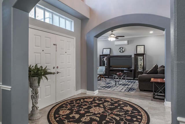 foyer featuring arched walkways, crown molding, a wall mounted AC, a ceiling fan, and baseboards