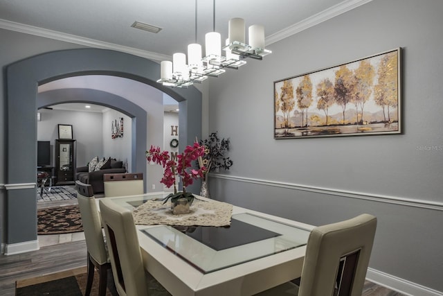 dining area with dark wood-style floors, arched walkways, a notable chandelier, visible vents, and ornamental molding