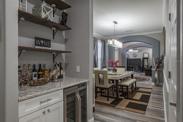 bar with wine cooler, arched walkways, decorative light fixtures, a dry bar, and light wood finished floors