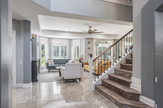 living area with stairs, marble finish floor, a ceiling fan, and baseboards