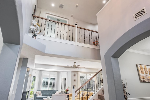 interior space featuring ornamental molding, visible vents, ceiling fan, and a towering ceiling