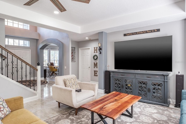 living area with arched walkways, stairway, a ceiling fan, and baseboards