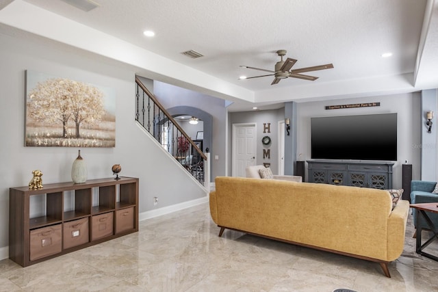 living room with ceiling fan, a raised ceiling, stairs, and baseboards