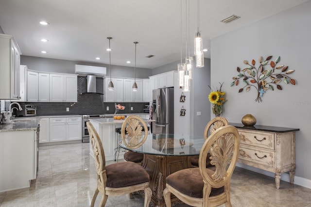 kitchen with visible vents, appliances with stainless steel finishes, white cabinetry, a kitchen island, and wall chimney range hood