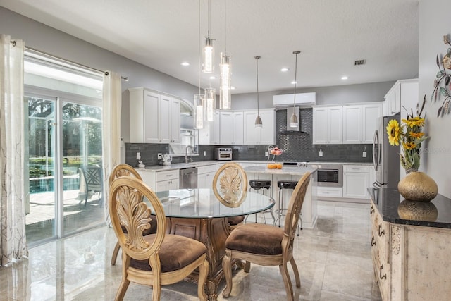 kitchen with wall chimney exhaust hood, decorative light fixtures, white cabinets, and a center island