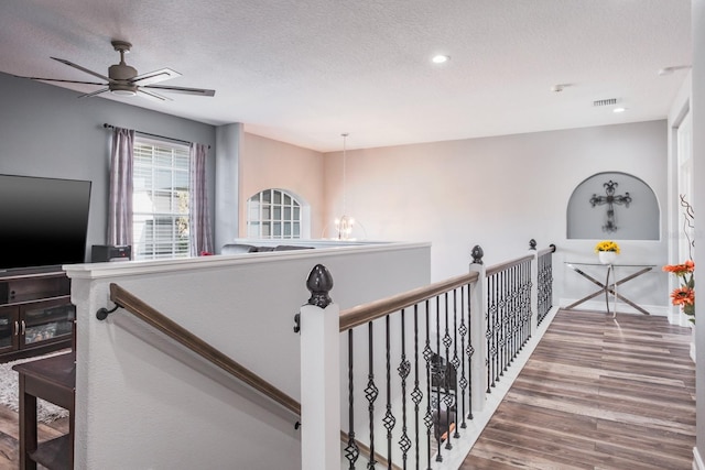 hall featuring visible vents, a textured ceiling, an upstairs landing, wood finished floors, and a chandelier