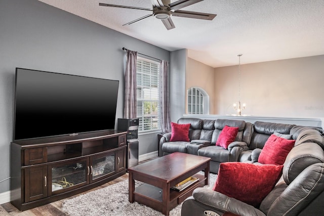 living area featuring baseboards, a textured ceiling, light wood finished floors, and ceiling fan with notable chandelier