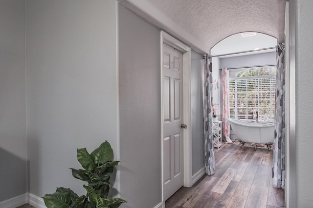 corridor with a textured ceiling, wood finished floors, and baseboards