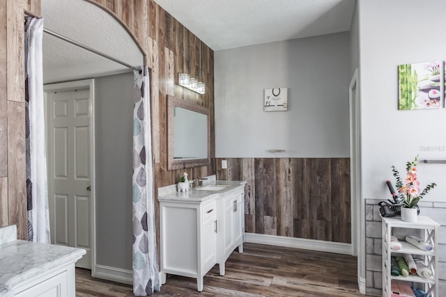 full bathroom featuring wood walls, vanity, a textured ceiling, and wood finished floors