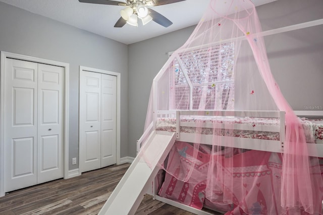 unfurnished bedroom featuring wood finished floors, ceiling fan, baseboards, and two closets