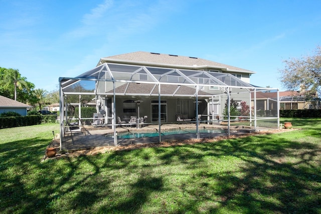 rear view of property with an outdoor pool, a lawn, a ceiling fan, a patio, and glass enclosure