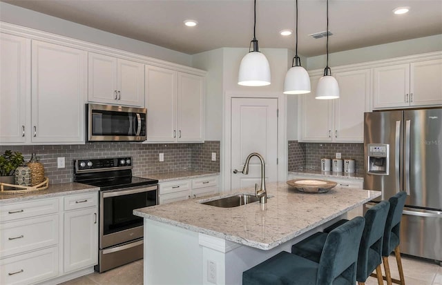 kitchen featuring stainless steel appliances, hanging light fixtures, an island with sink, and white cabinets