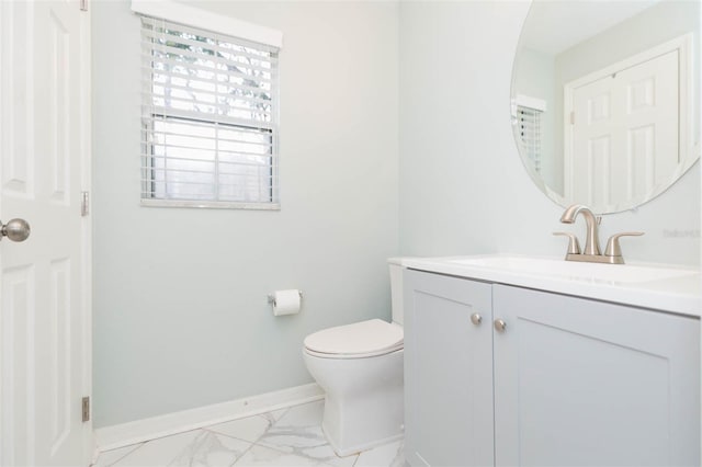 bathroom with toilet, marble finish floor, vanity, and baseboards