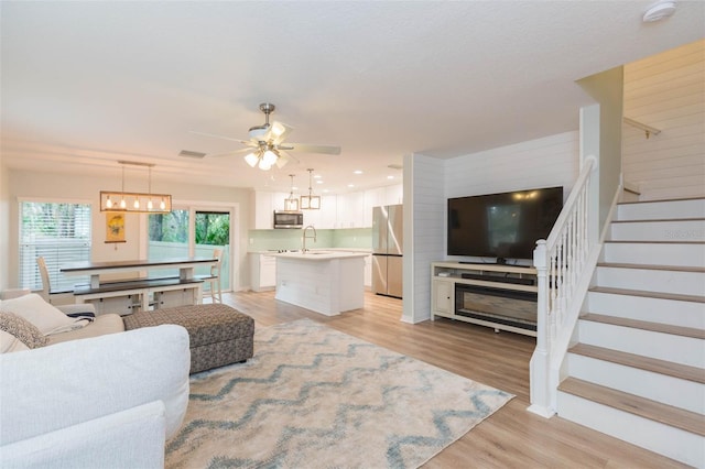 living room with recessed lighting, ceiling fan with notable chandelier, visible vents, stairs, and light wood finished floors