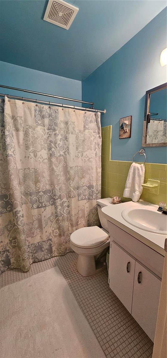 bathroom with visible vents, wainscoting, tile patterned floors, vanity, and tile walls