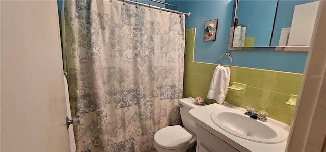 full bath featuring toilet, a wainscoted wall, a shower with shower curtain, vanity, and tile walls