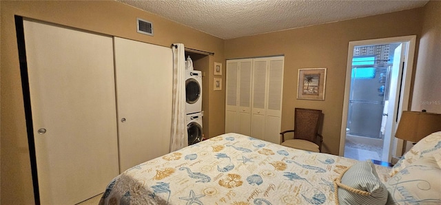 bedroom featuring a textured ceiling, multiple closets, visible vents, and stacked washer / drying machine