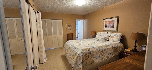 bedroom featuring light carpet, a textured ceiling, and two closets