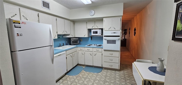 kitchen with white appliances, visible vents, a textured ceiling, light floors, and a sink