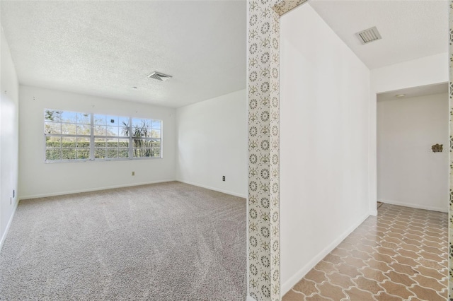 carpeted spare room with a textured ceiling, visible vents, and baseboards