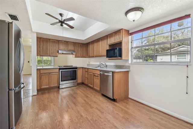 kitchen with a raised ceiling, light wood-style flooring, appliances with stainless steel finishes, a textured ceiling, and under cabinet range hood