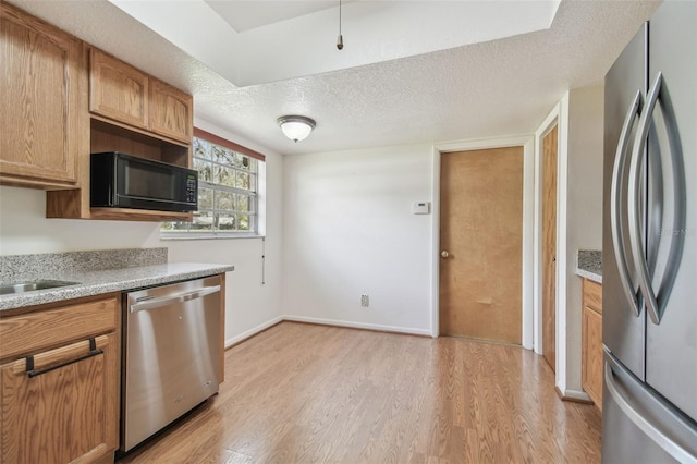 kitchen with baseboards, appliances with stainless steel finishes, light countertops, a textured ceiling, and light wood-type flooring