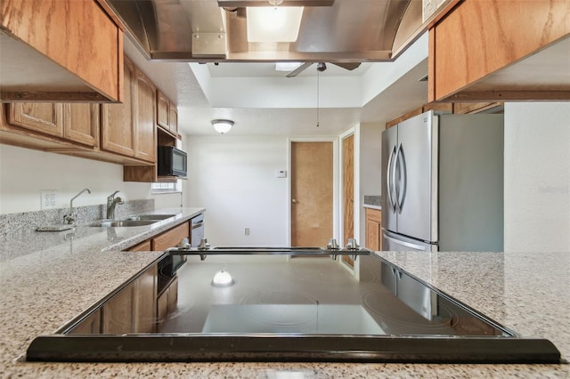 kitchen featuring light stone counters, freestanding refrigerator, brown cabinets, and a sink