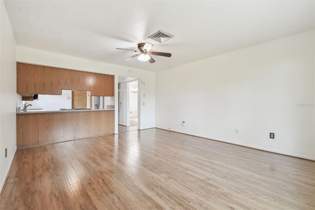 unfurnished living room with a sink, visible vents, baseboards, a ceiling fan, and light wood finished floors