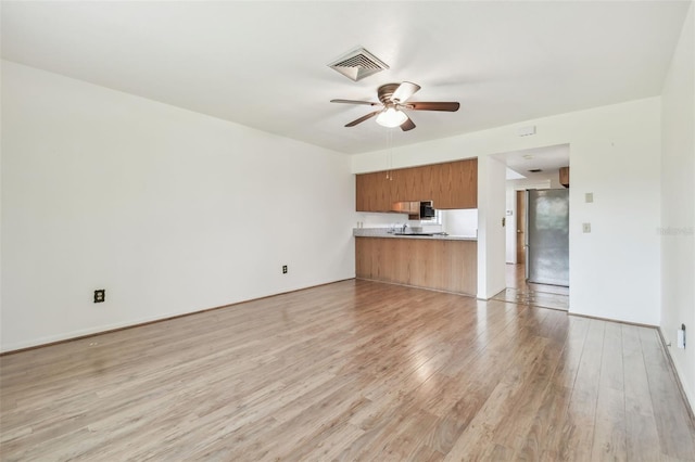 unfurnished living room with ceiling fan, light wood finished floors, visible vents, and baseboards