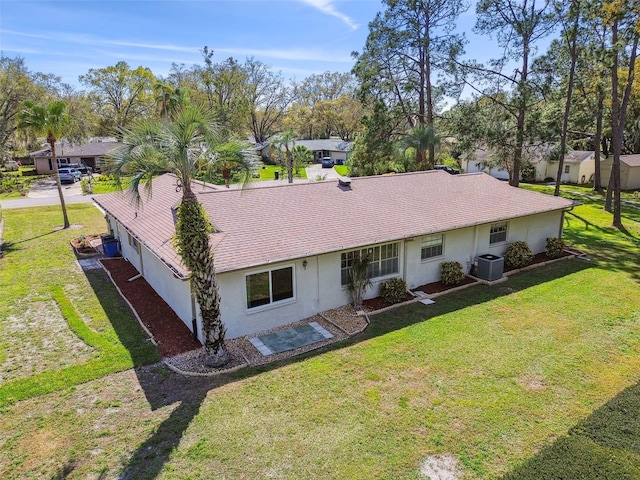 rear view of property featuring a yard, central AC unit, a shingled roof, and stucco siding