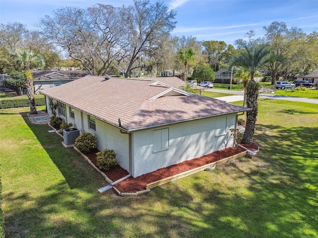 view of side of home featuring cooling unit, roof with shingles, a lawn, a residential view, and stucco siding