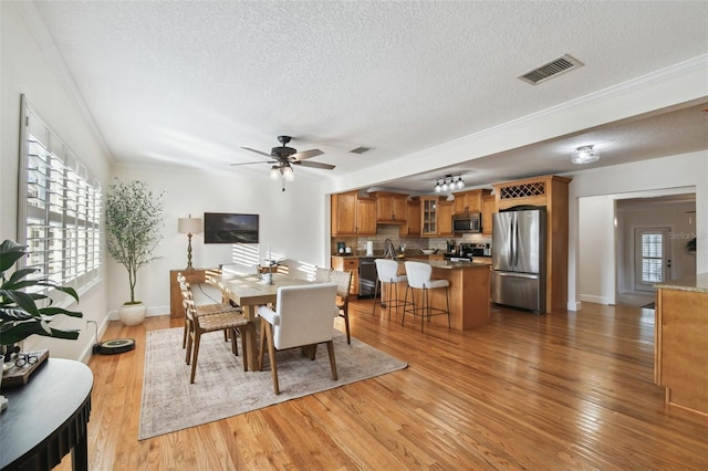 dining room with visible vents, ceiling fan, ornamental molding, wood finished floors, and a textured ceiling