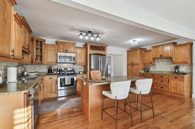 kitchen with brown cabinetry, a kitchen island, glass insert cabinets, appliances with stainless steel finishes, and a sink