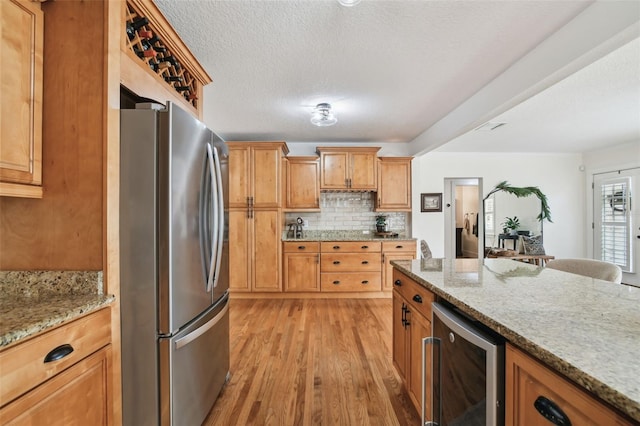 kitchen featuring light stone counters, wine cooler, light wood-style flooring, decorative backsplash, and freestanding refrigerator