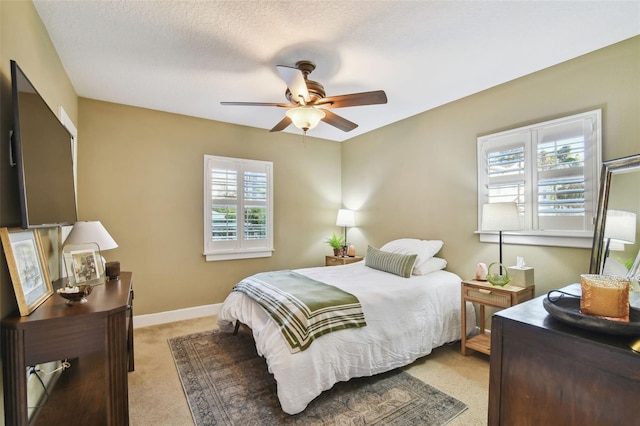 bedroom featuring light carpet, ceiling fan, baseboards, and a textured ceiling