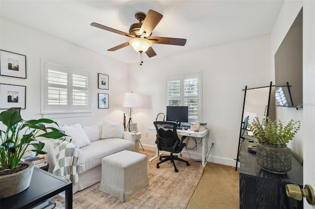 office space featuring light carpet, a ceiling fan, baseboards, and a wealth of natural light