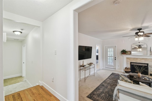 living area with a textured ceiling, baseboards, a tiled fireplace, and light colored carpet