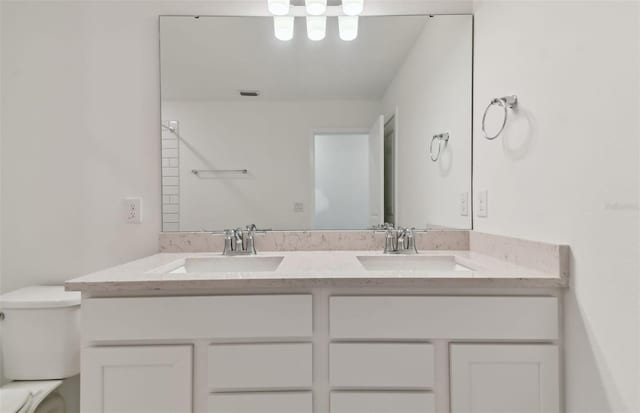 full bath with visible vents, a sink, toilet, and double vanity