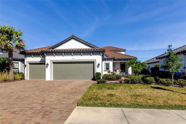 mediterranean / spanish-style house featuring a garage, a tiled roof, decorative driveway, a front yard, and stucco siding