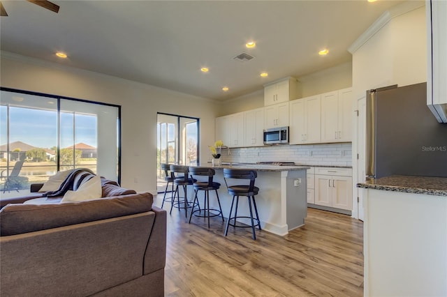 kitchen with stainless steel appliances, visible vents, open floor plan, white cabinetry, and an island with sink