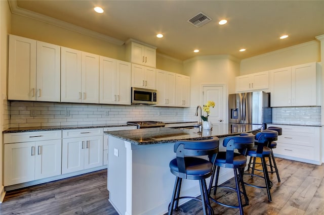 kitchen featuring appliances with stainless steel finishes, a center island with sink, visible vents, and white cabinets